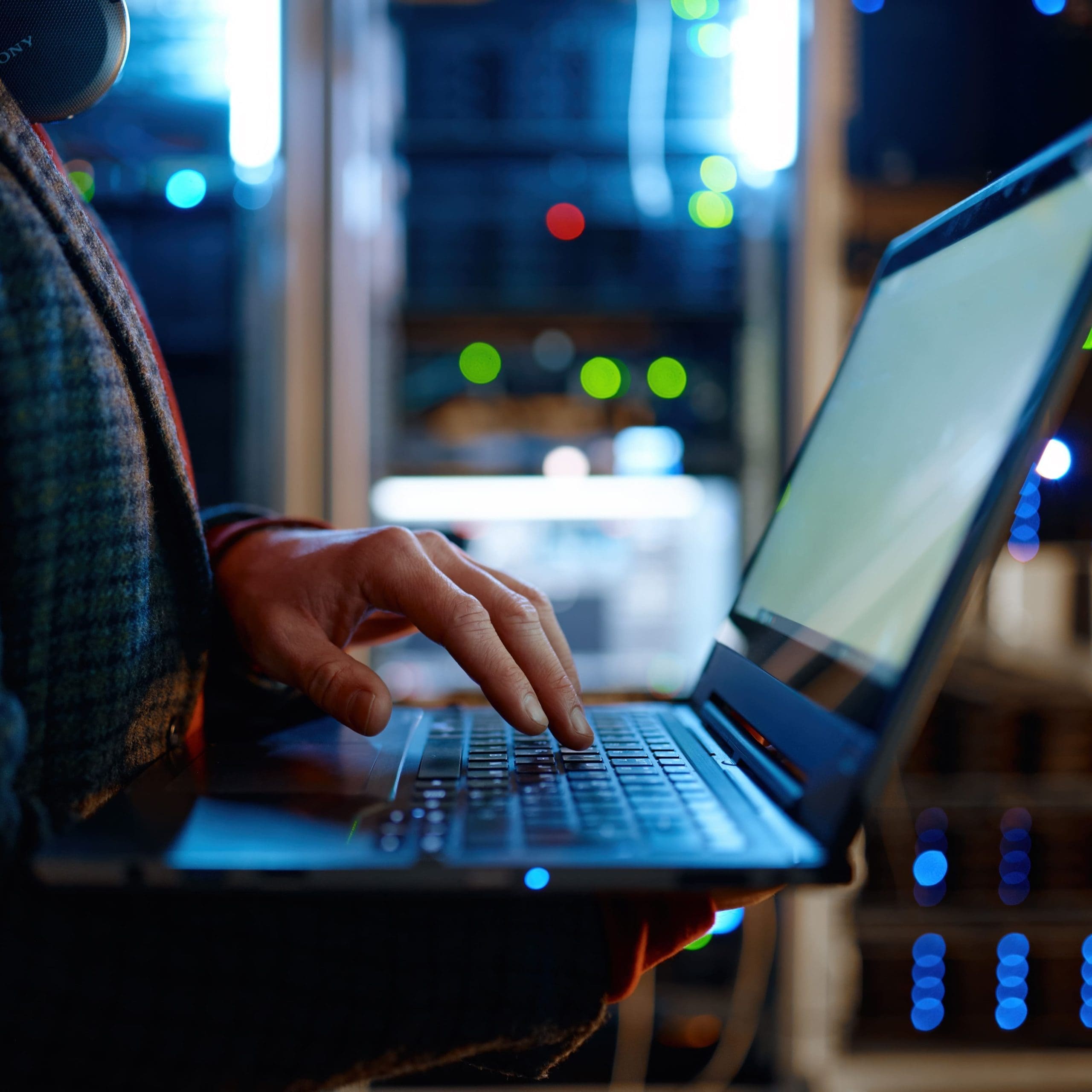 IT technician checking the servers vitals using laptop computer. Male support agent working in a dark network server room